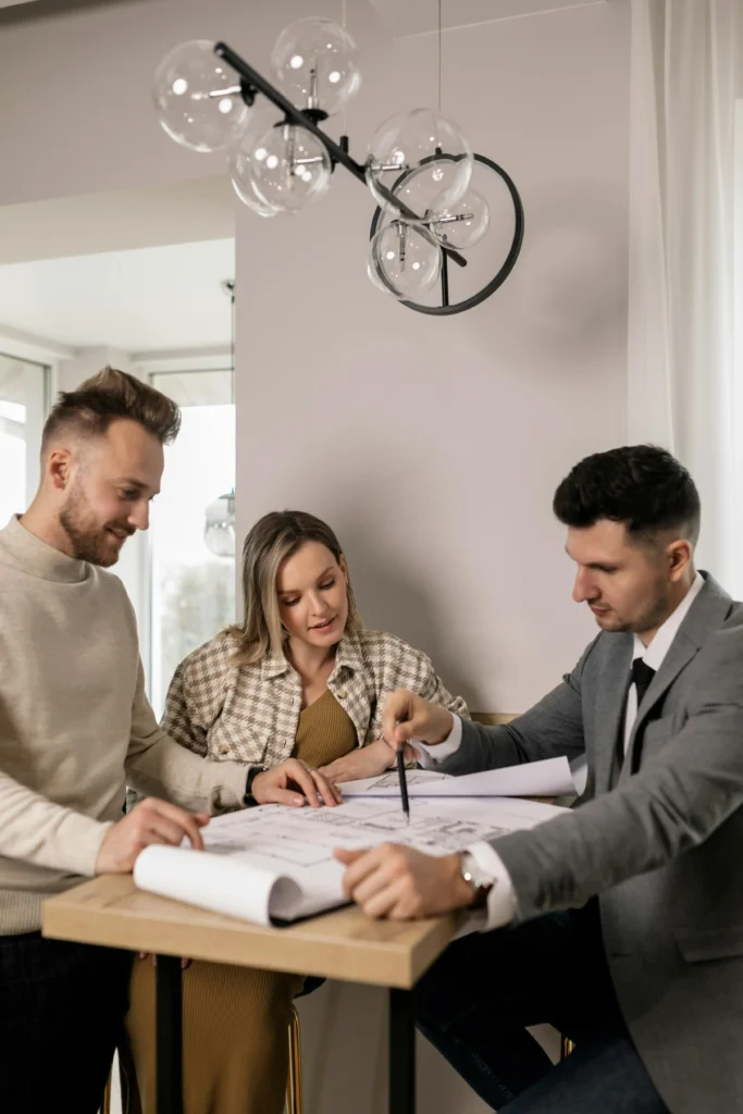 Three individuals engaged in discussion at a table, examining a blueprint together.