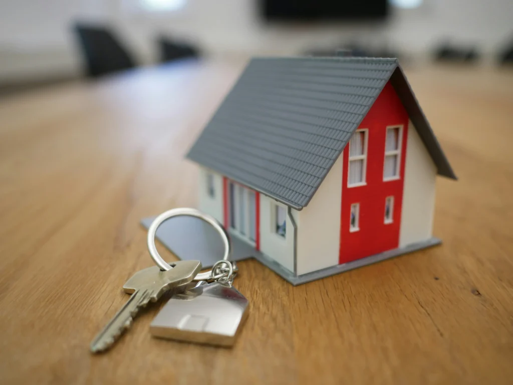 A house model placed on a table alongside a set of keys, symbolizing home ownership and real estate.